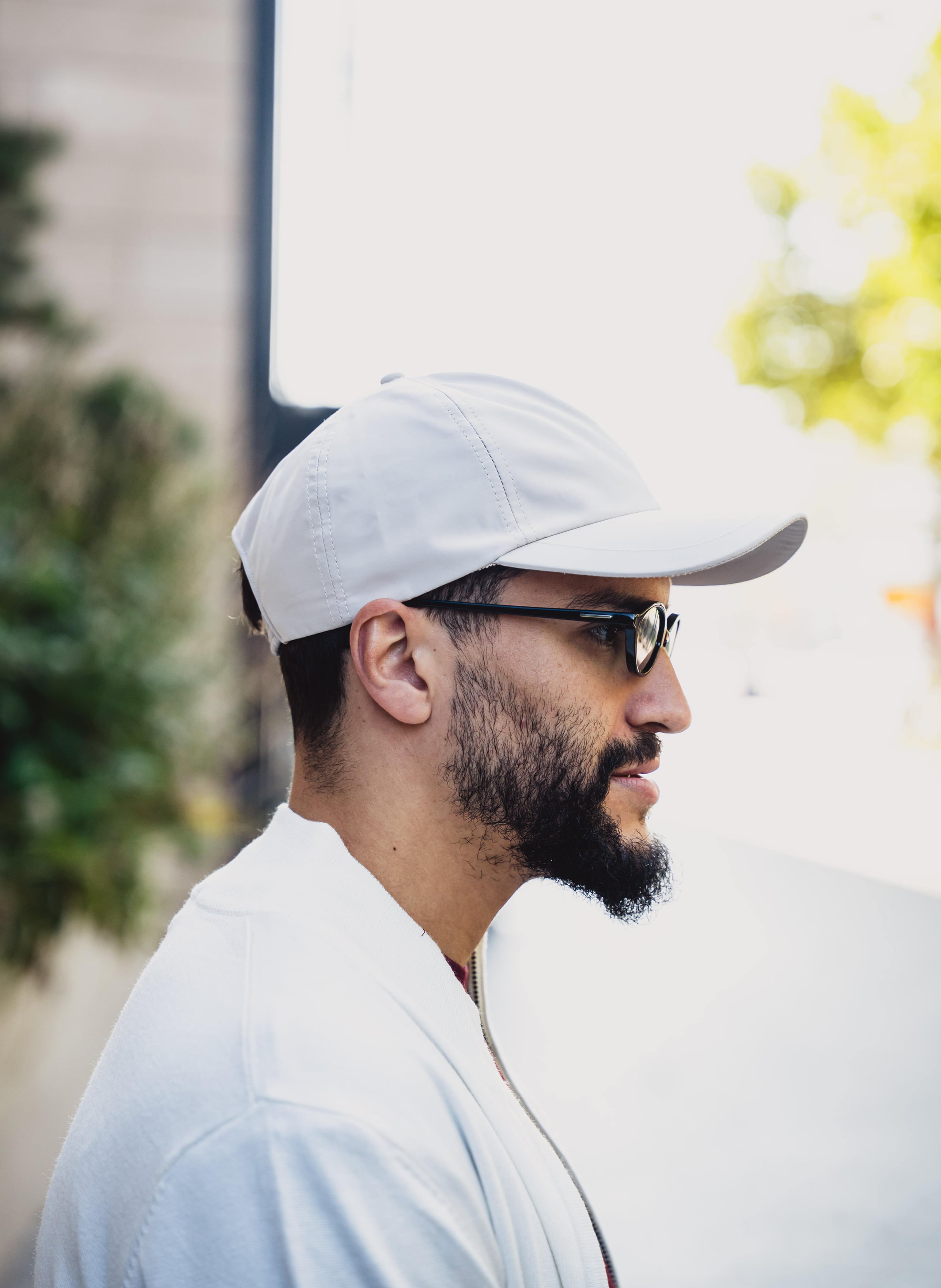 Man met een lichte pet en bril in zijaanzicht, buiten staand in fel zonlicht.