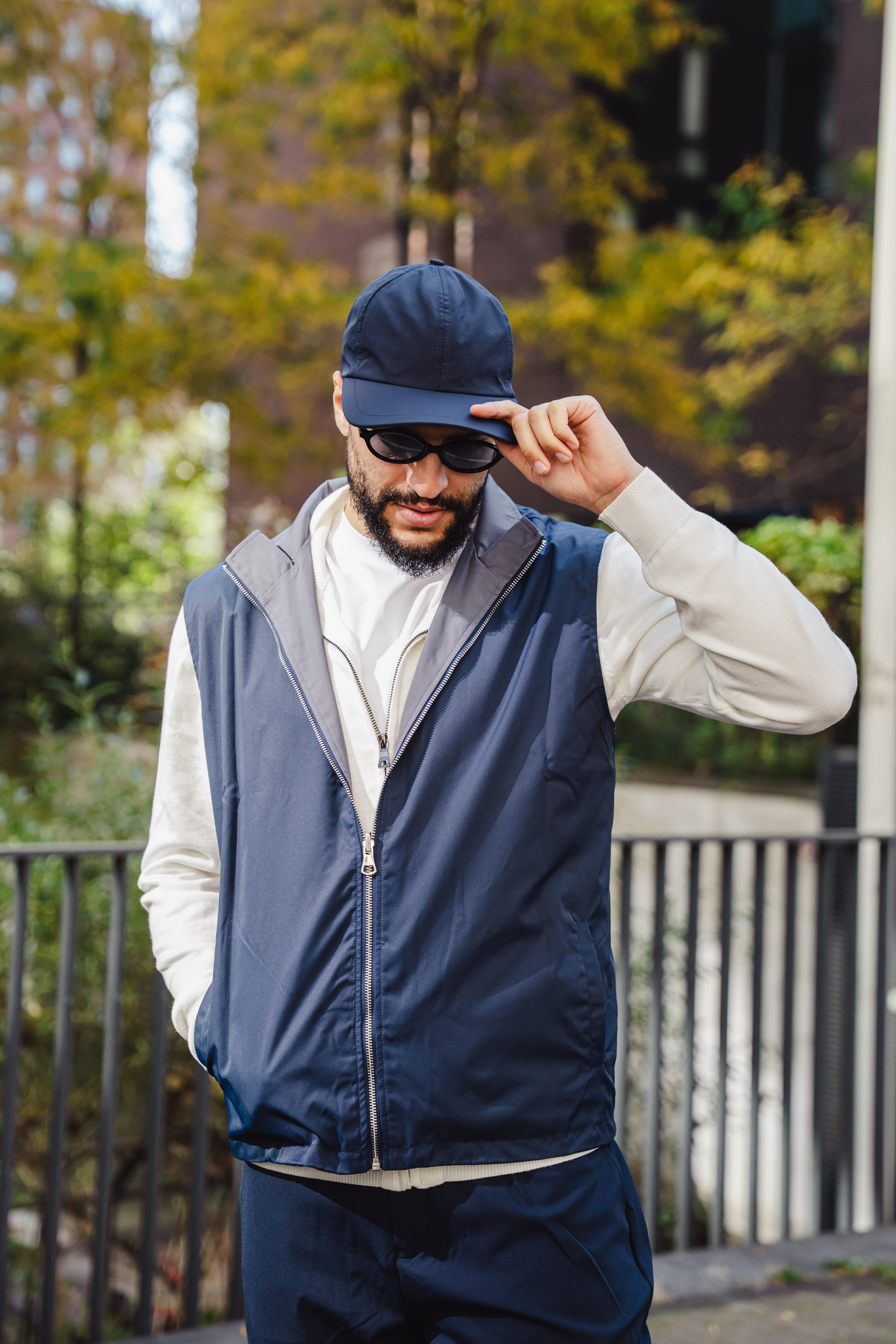 Man in een donkerblauwe bodywarmer en pet die zijn zonnebril rechtzet terwijl hij buiten staat.